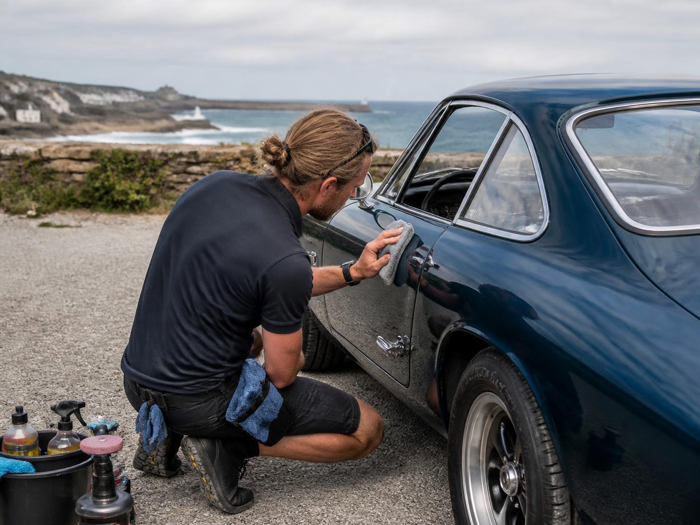 A mobile detailer carefully polishing a classic car near the Cornish coast